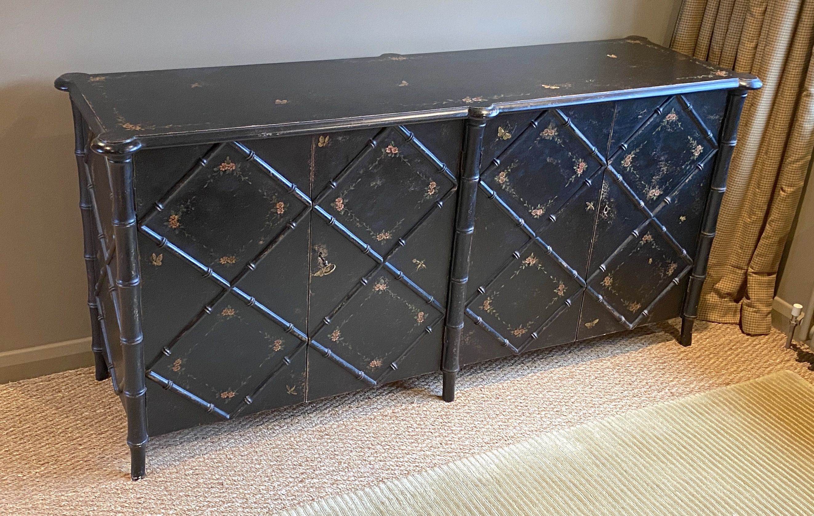 A black painted simulated bamboo low cabinet, with folding doors and floral painted decoration, width 180cm depth 55cm height 86cm, made to be used as a freestanding cupboard